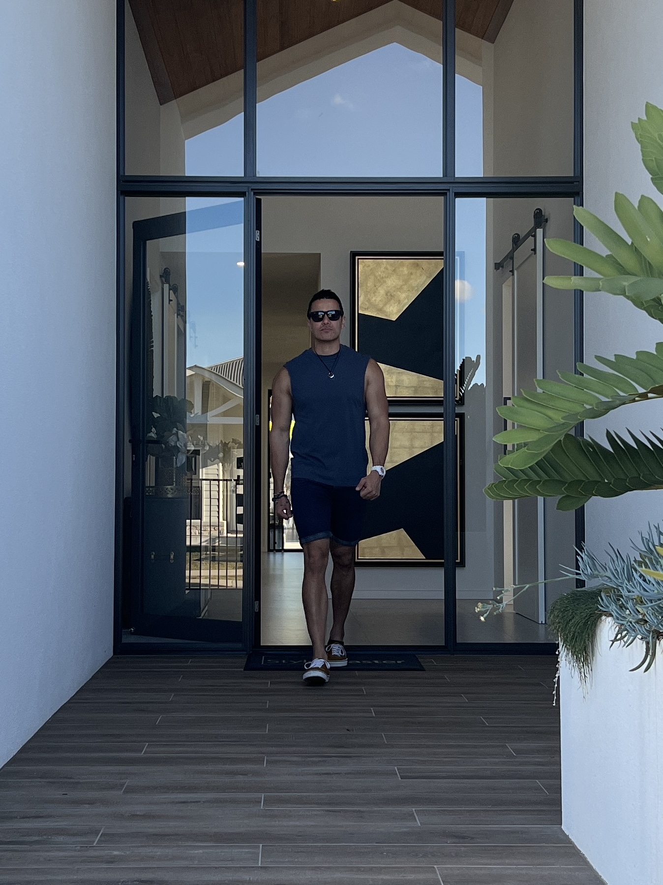 Casey Barnard wearing sunglasses and a navy sleeveless top, walking through tall glass doors.